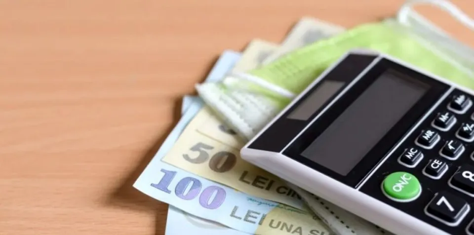 Un calculator de birou alb cu butoane negre este așezat peste câteva bancnote de lei și o mască medicală de culoare verde.