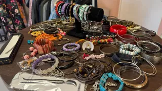Multe brățări colorate, de diverse materiale și culori, sunt întinse pe o masă circulară de culoare maro.