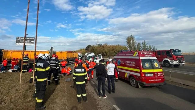 Pompieri în uniforme galben-negru și personal medical stau lângă un vehicul de intervenție roșu și un camion galben pe marginea unei drumuri.