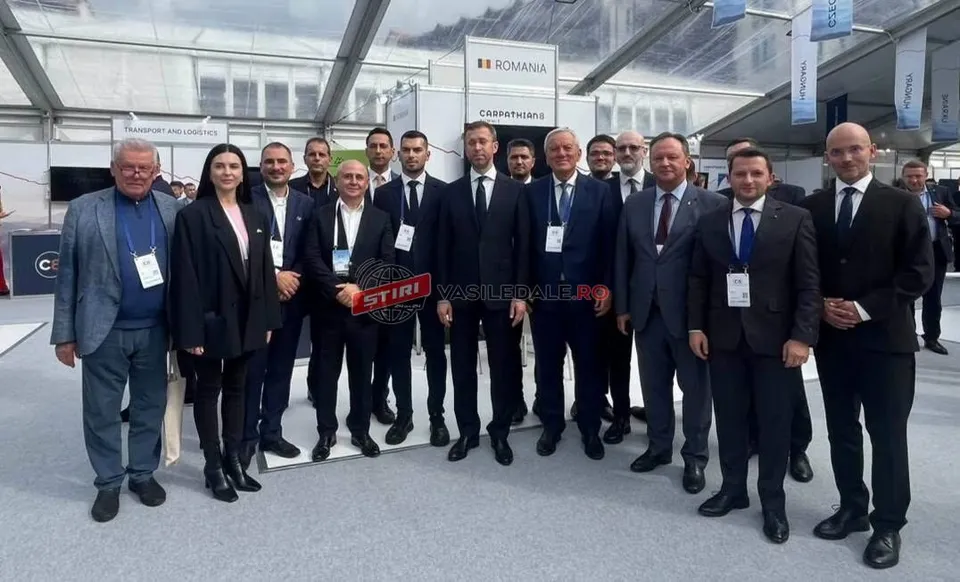 Un grup de persoane îmbrăcate în haine office stă în picioare sub o structură de tip cort, în fața unor panouri informative cu text și logo-uri.