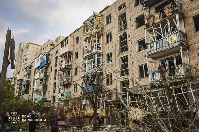 Un bloc de apartamente cu ferestre sparte și balcoane distruse prezintă resturi de materiale și ramuri de copaci în fața clădirii.