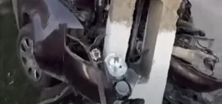 Un autoturism de culoare închisă prezintă partea frontală și roata stângă puternic avariate lângă un obiect vertical de culoare deschisă.