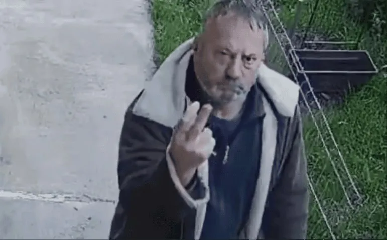 Un bărbat cu barbă și păr scurt poartă o jachetă închisă la culoare cu căptușeală albă și ridică mâna stângă în semn de victorie.