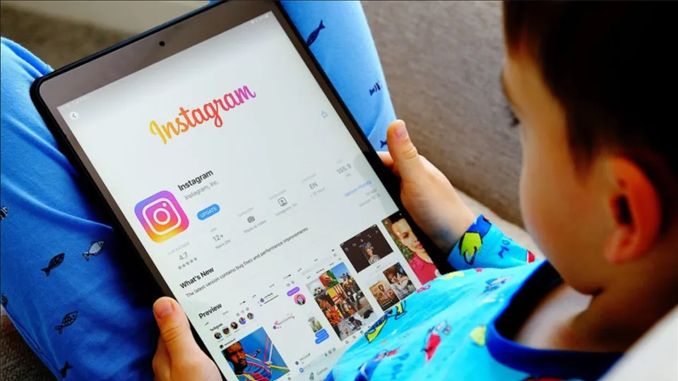 Un copil ține o tabletă pe care este afișată pagina de profil a unei rețele sociale, fiind văzut din profil.