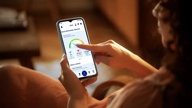 O persoană ține un smartphone și atinge ecranul pe care se afișează un grafic circular colorat și diverse pictograme într-o aplicație mobilă.