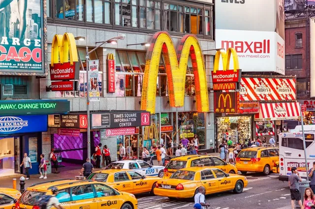Un semn McDonald's galben este montat pe o clădire de lângă o stradă aglomerată cu taxiuri și mulțime de oameni.