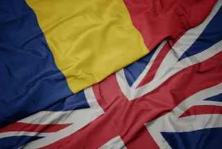 Două steaguri, unul cu dungi verticale albastru, galben și roșu și unul cu modelul Union Jack, sunt întrepătrunse și prezintă pliuri de material textil.