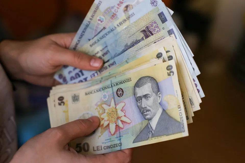 Două mâini țin un teanc de bancnote de cincizeci de lei românești.