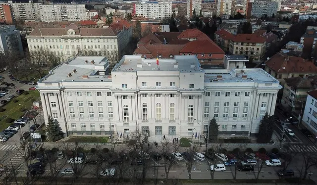 O vedere aeriană a unei clădiri albe cu ferestre multiple, înconjurată de alte construcții urbane și copaci fără frunze.