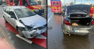 Două autoturisme avariate sunt parcate pe un drum umed, lângă o ambulanță roșie și albă.