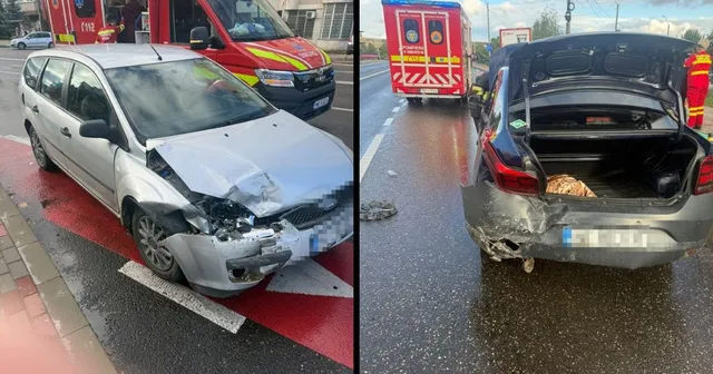 Două autoturisme avariate sunt parcate pe un drum umed, lângă o ambulanță roșie și albă.