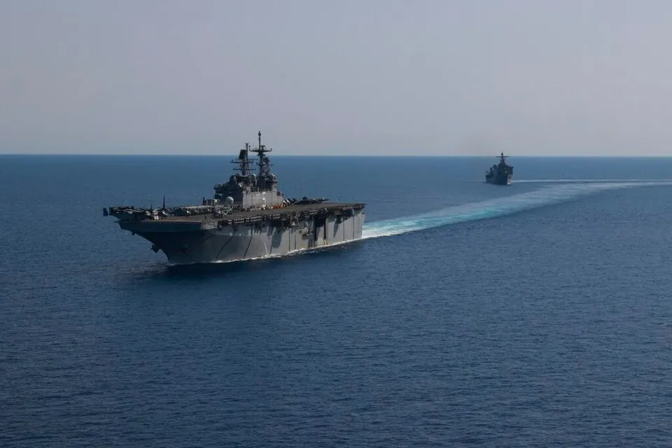 Două nave militare gri navighează pe o suprafață de apă albastră sub un cer senin.