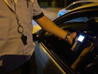 O persoană în uniformă ține un aparat de testare alcoolemiei în interiorul unui autoturism de la nivelul ferestrei deschise.