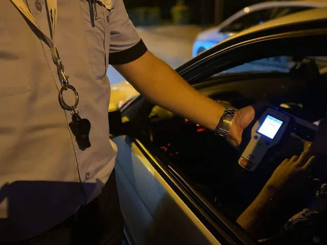 O persoană în uniformă ține un aparat de testare alcoolemiei în interiorul unui autoturism de la nivelul ferestrei deschise.