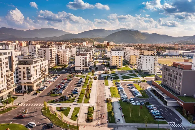 O vedere aeriană asupra unui cartier urban cu clădiri rezidențiale de înălțime medie, parcuri verzi și mașini parcate pe străzi și în parcări.