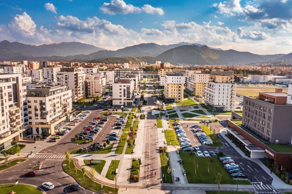 O vedere aeriană asupra unui cartier urban cu clădiri rezidențiale de înălțime medie, parcuri verzi și mașini parcate pe străzi și în parcări.