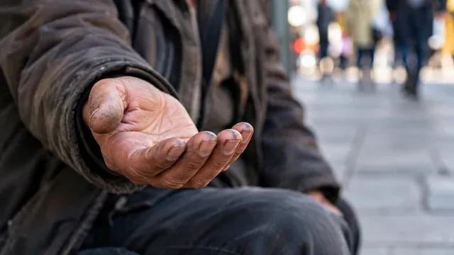 O persoană purtând o jachetă maro stă cu palma întinsă în față pe un trotuar.