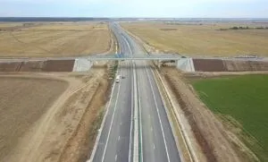 O autostradă cu mai multe benzi traversează un peisaj agricol plat sub un cer înnorat.