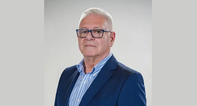 Un bărbat cu părul alb și ochelari cu rame negre poartă un sacou albastru peste o cămașă cu dungi subțiri albastre și albe.