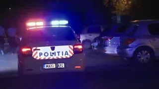 Spatele unei mașini cu inscripția POLITIA și lumini de avertizare albastre și roșii este vizibil pe un drum noaptea lângă alte vehicule.