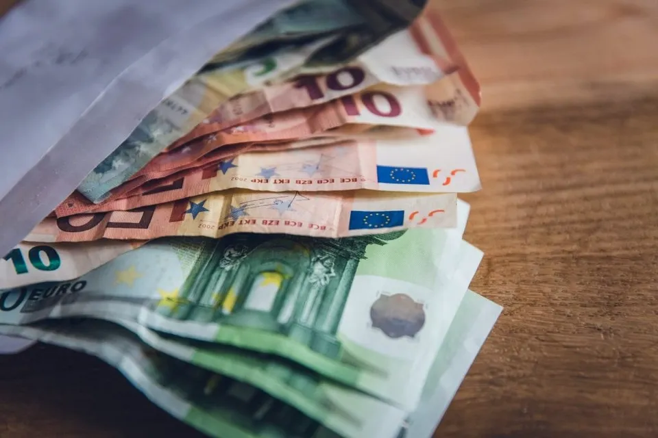Bani euro de diferite valori sunt așezați într-un plic deschis pe o suprafață de lemn.