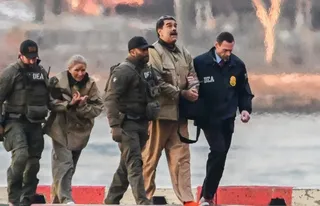 Patru persoane merg pe un drum, fiind însoțite de doi bărbați purtând veste cu inscripția DEA.