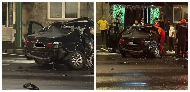 Un autoturism negru este situat pe carosabil, având partea din spate și acoperișul puternic deformate, în timp ce persoane stau în apropiere.
