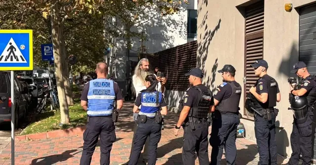 Șase polițiști în uniformă albastră și neagră stau pe un trotuar lângă o clădire, cu spatele sau profilul spre cameră.