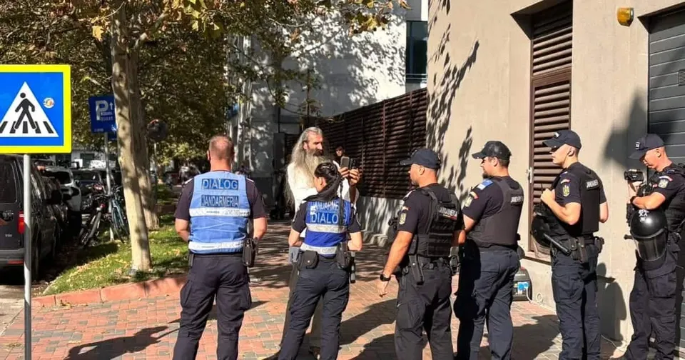 Șase polițiști în uniformă albastră și neagră stau pe un trotuar lângă o clădire, cu spatele sau profilul spre cameră.