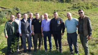 Un grup de nouă bărbați stă în picioare pe un teren verde în fața unui deal împădurit.