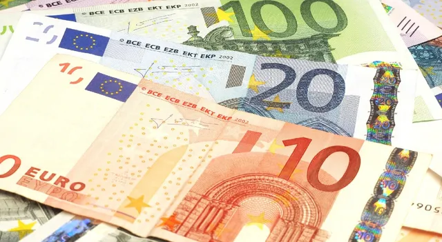 Bancoile euro de 10, 20 și 100 de euro sunt împrăștiate pe o suprafață deschisă la culoare.