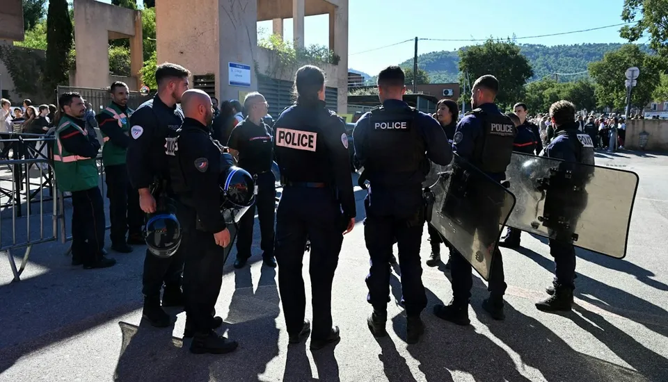 Mai mulți polițiști în uniforme în plantea întregului corp stau pe un drum, unii purtând scuturi de protecție și echipament tactic.