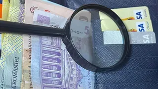 O lupă neagră este așezată peste mai multe bancnote de lei românești întinse pe o suprafață textilă albastră.
