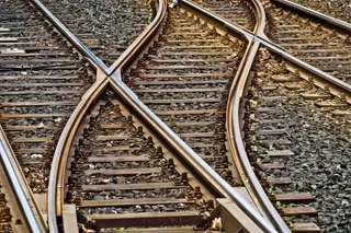 Mai multe șine de tren metalice se intersectează pe pat de pietriș și traversee de lemn.