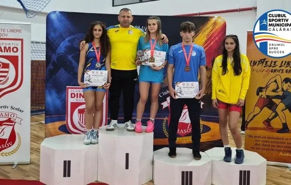 Cinci tineri stau pe podiumuri albe în fața unui panou colorat, purtând medalii și certificate în mâini.