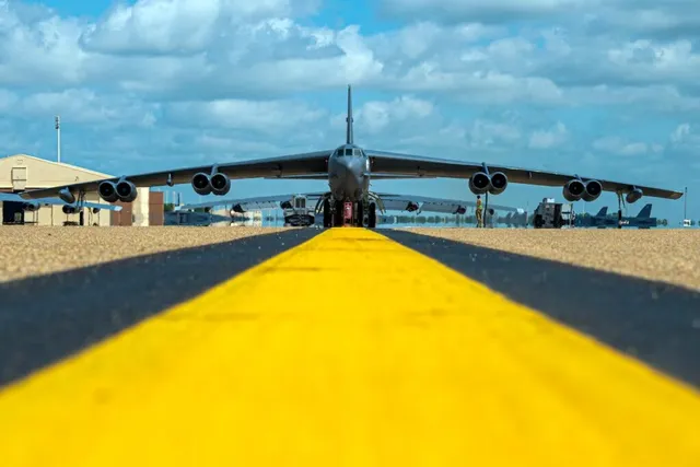 Un avion de mari dimensiuni cu patru motoare este poziționat pe o pistă de decolare sub un cer cu nori pufoși.