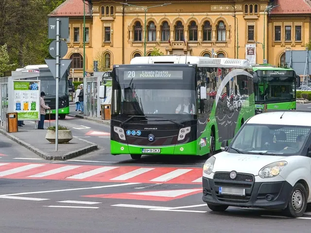 Un autobuz verde și alb circulă pe un drum lângă un punct de oprire, în timp ce o mașină albă este parcată în prim-plan.