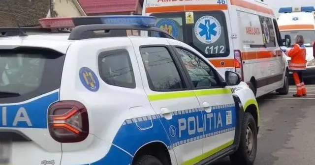 O mașină de poliție albă și albastră este parcată pe un drum lângă o ambulanță albă cu inscripții medicale și un om în vestă portocalie.