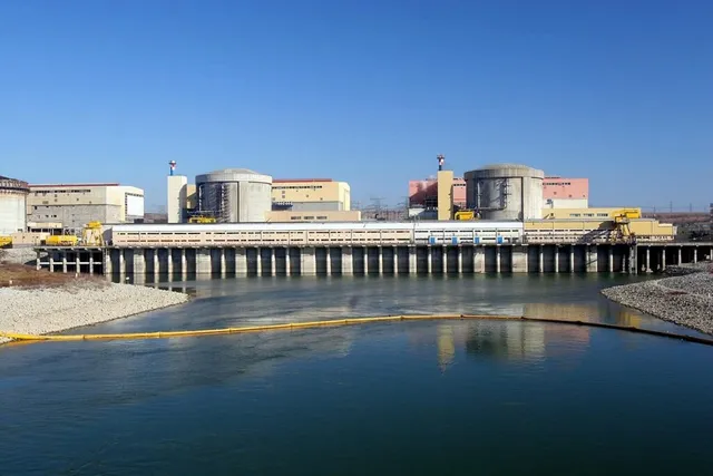 Nuclear power plant with two cooling towers beside a river under a clear blue sky.
