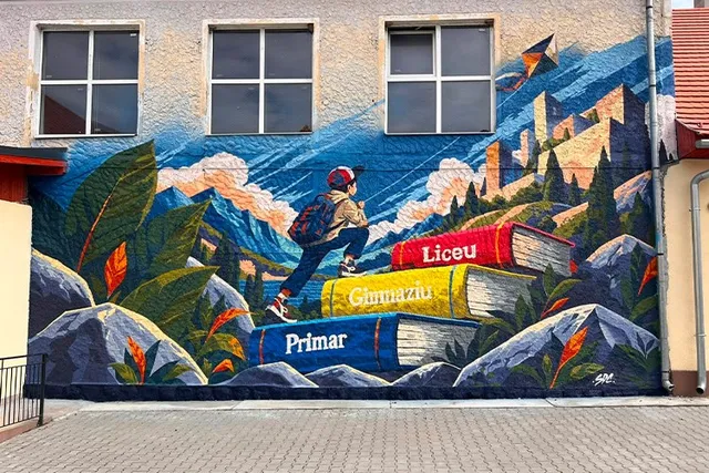 Un mural colorat pe un perete de clădire prezintă cărți mari, munți, vegetație și o figură umană cu rucsac în fața unui peisaj montan.