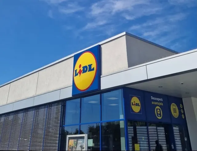 Fațada unei clădiri comerciale cu panouri de sticlă albastră și un panou publicitar galben cu un logo pe fundal albastru.