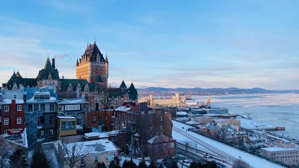 O vedere panoramică asupra unui oraș cu clădiri de stil istoric, situat pe malul unui fluviu sub un cer senin.