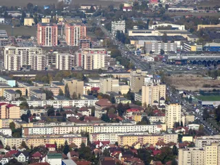 O vedere aeriană asupra unui oraș cu numeroase clădiri rezidențiale de înălțime medie și înaltă, străzi și zone cu vegetație dispersată.