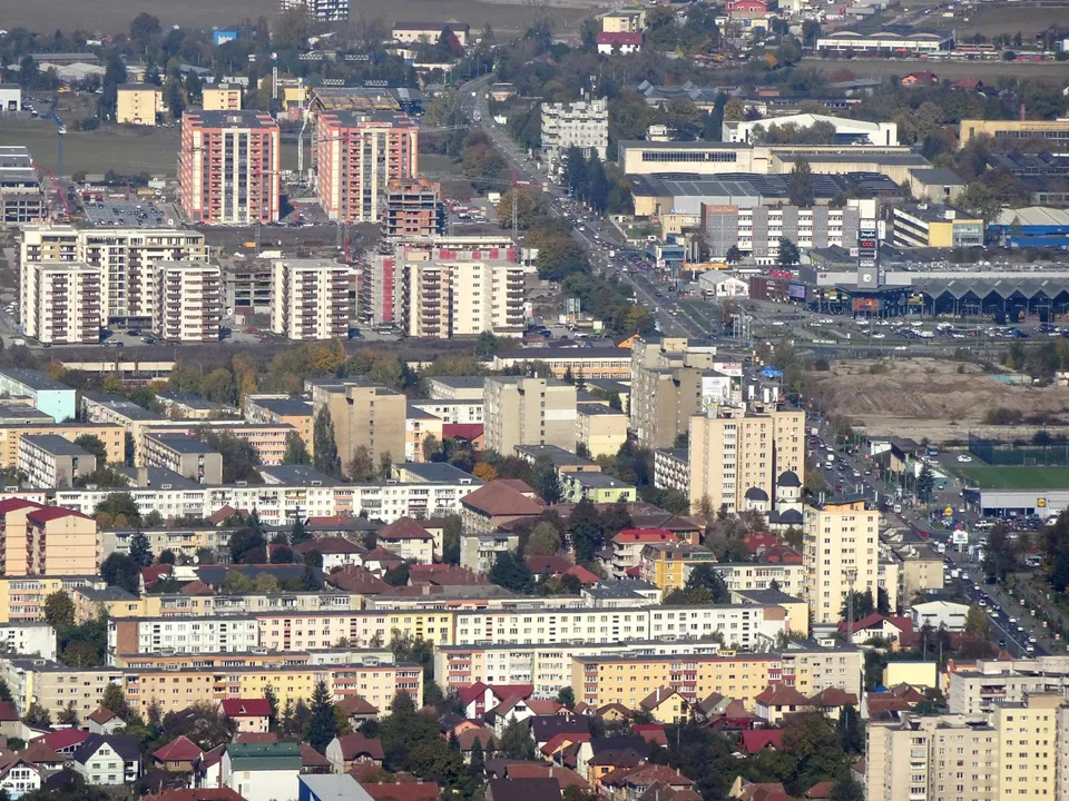 O vedere aeriană asupra unui oraș cu numeroase clădiri rezidențiale de înălțime medie și înaltă, străzi și zone cu vegetație dispersată.