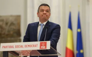 Un bărbat într-un costum albastru și cravată deschisă stă în spatele unui podium alb cu inscripția PARTIDUL SOCIAL DEMOCRAT.
