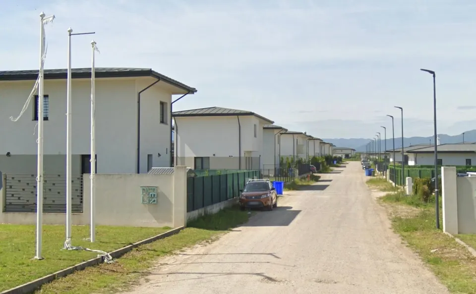 O serie de case albe cu acoperișuri înclinat sunt situate de-a lungul unui drum de țărână sub un cer înnorat.