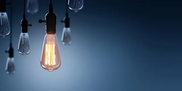Mai multe becuri suspendate de cabluri sunt vizibile pe un fundal albastru, dintre acestea unul este aprins.