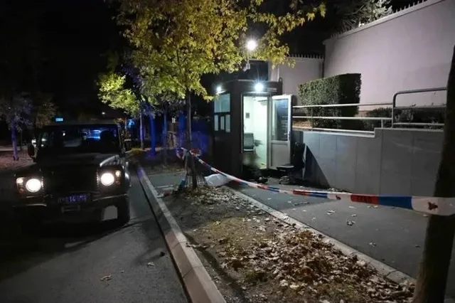 O cabine de pază iluminată noaptea, înconjurată de o bandă polițială roșie și albastră, cu un vehicul parcat în stânga.