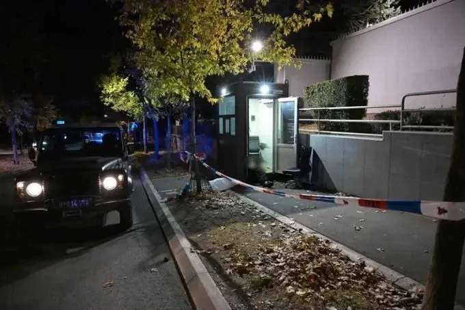 O cabine de pază iluminată noaptea, înconjurată de o bandă polițială roșie și albastră, cu un vehicul parcat în stânga.