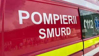 Un vehicul de serviciu roșu prezintă inscripții albe cu textul POMPIERII SMURD și numărul de urgență 112 pe lateral.